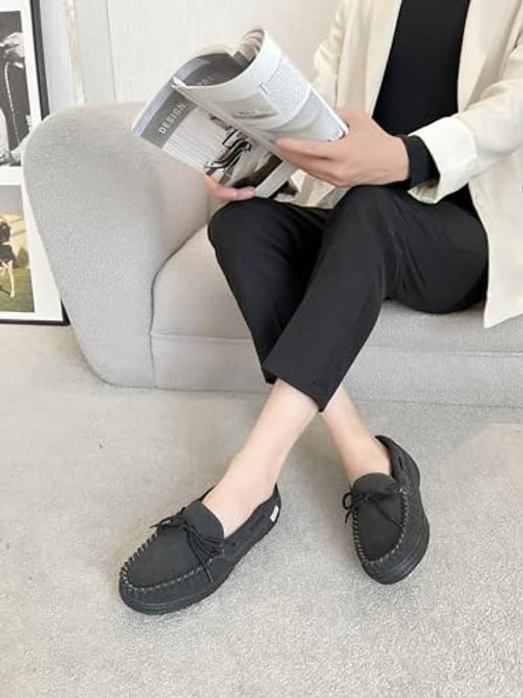 Man wearing charcoal gray lace-up moccasin slippers on indoor carpet flooring.