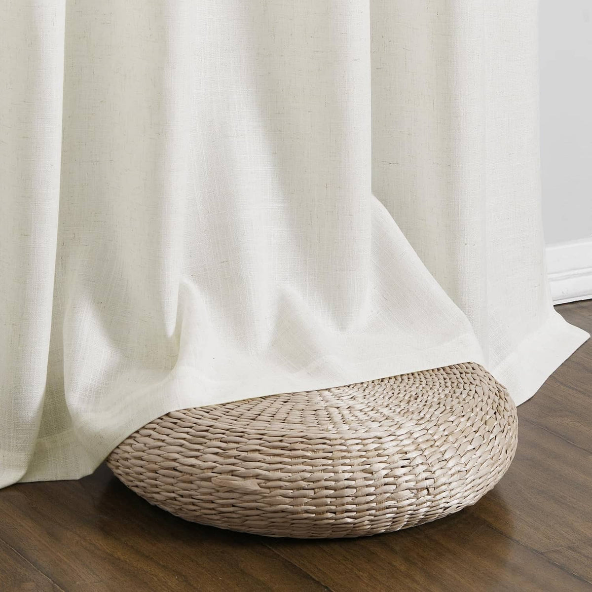 Natural linen curtain with straight hem and soft drape corner beside woven basket