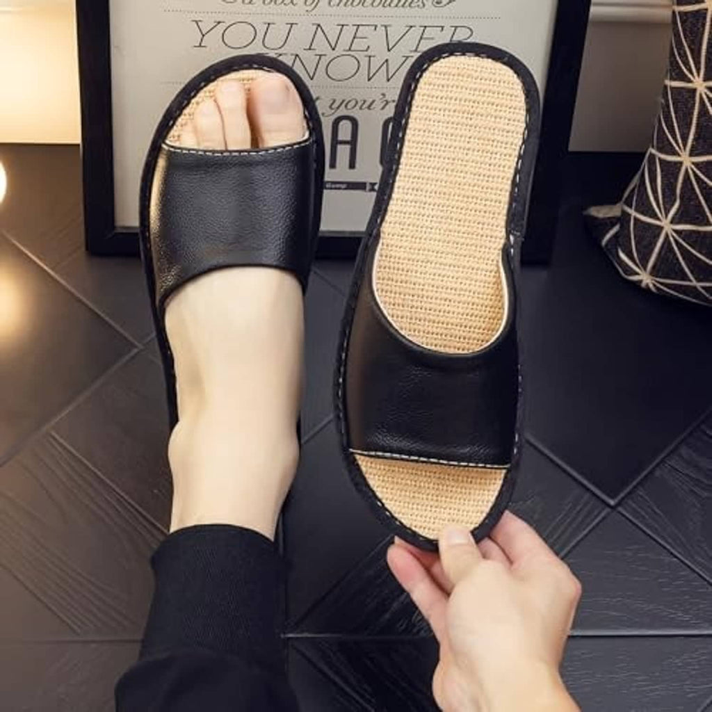 Black open-back leather house slippers with beige woven footbed on feet.