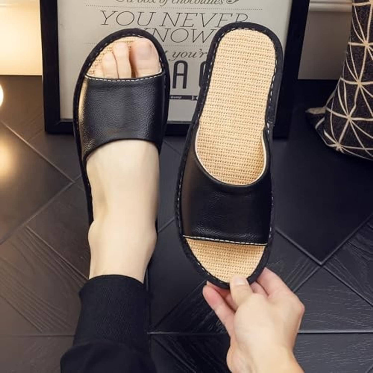 Black open-back leather house slippers with beige woven footbed on feet.