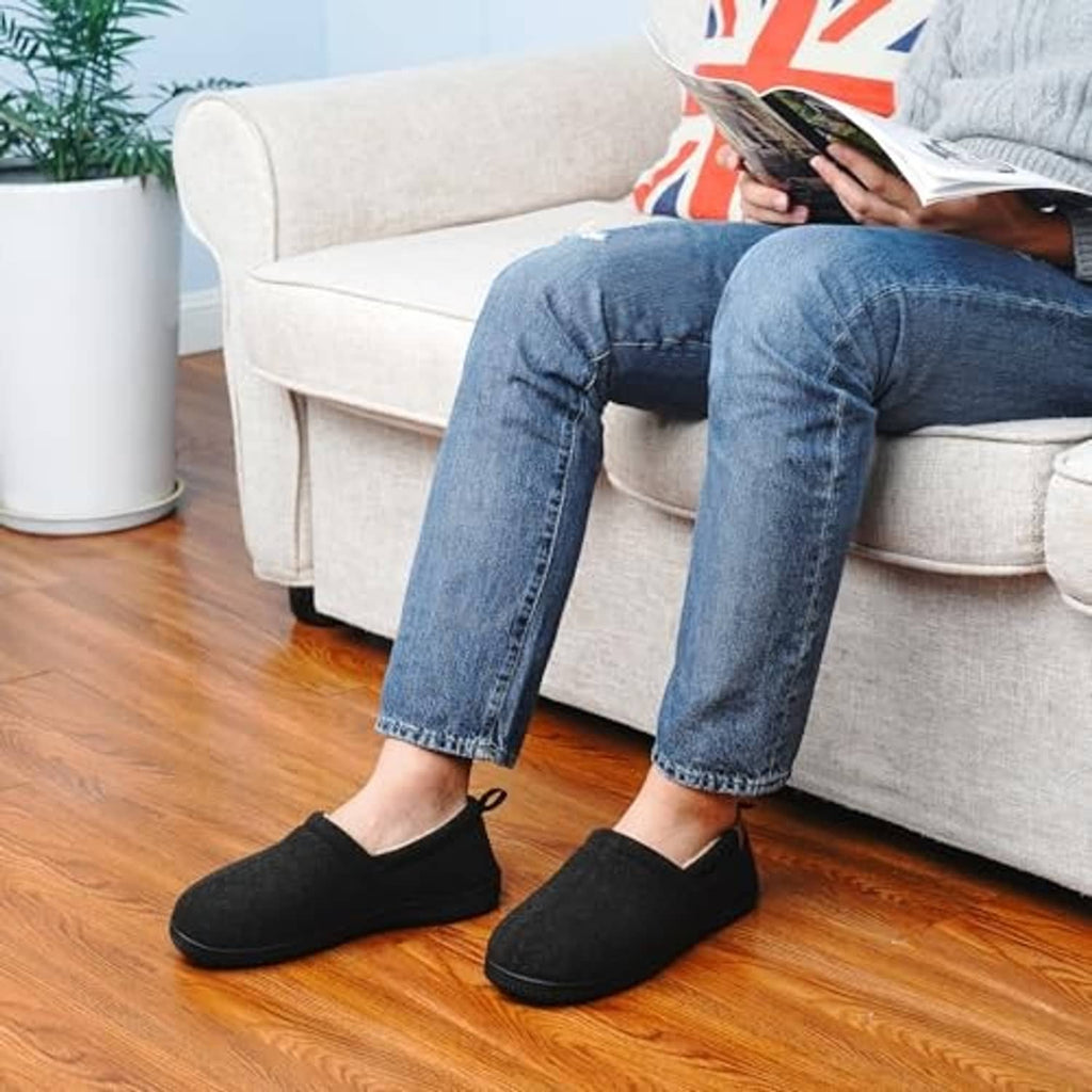 Men's black slippers worn with denim jeans, plush lining visible at the collar