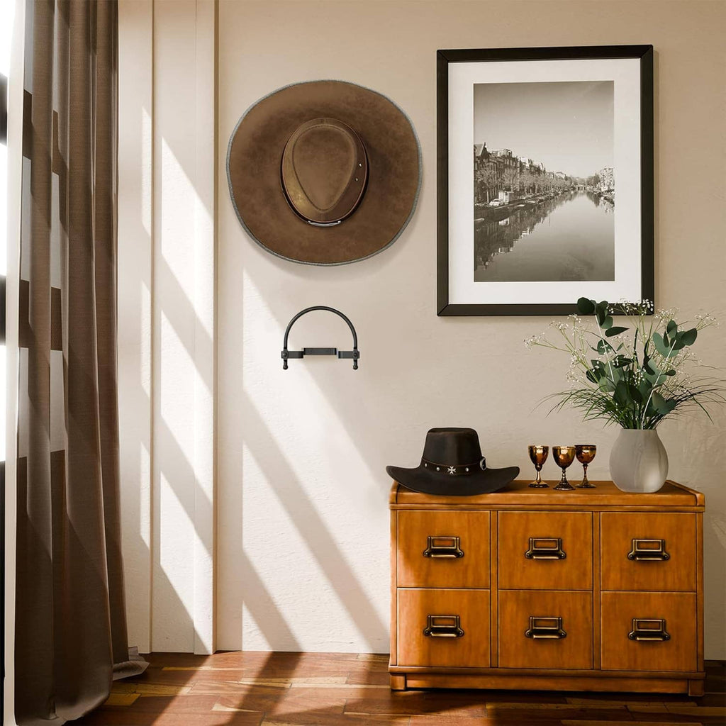 Wall-mounted hat holder with black curved hooks holding a brown cowboy hat