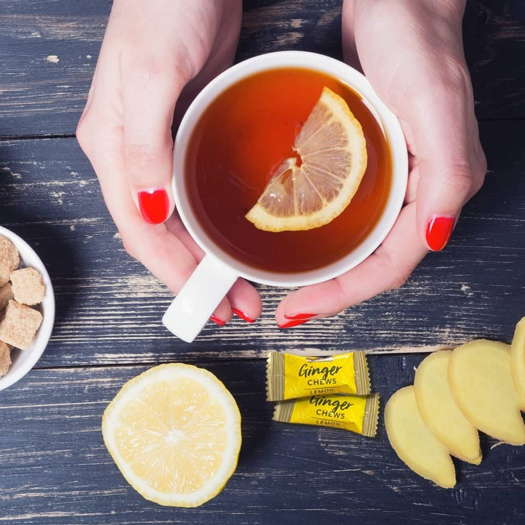 Hands holding a cup of tea with lemon slice and ginger chews packets