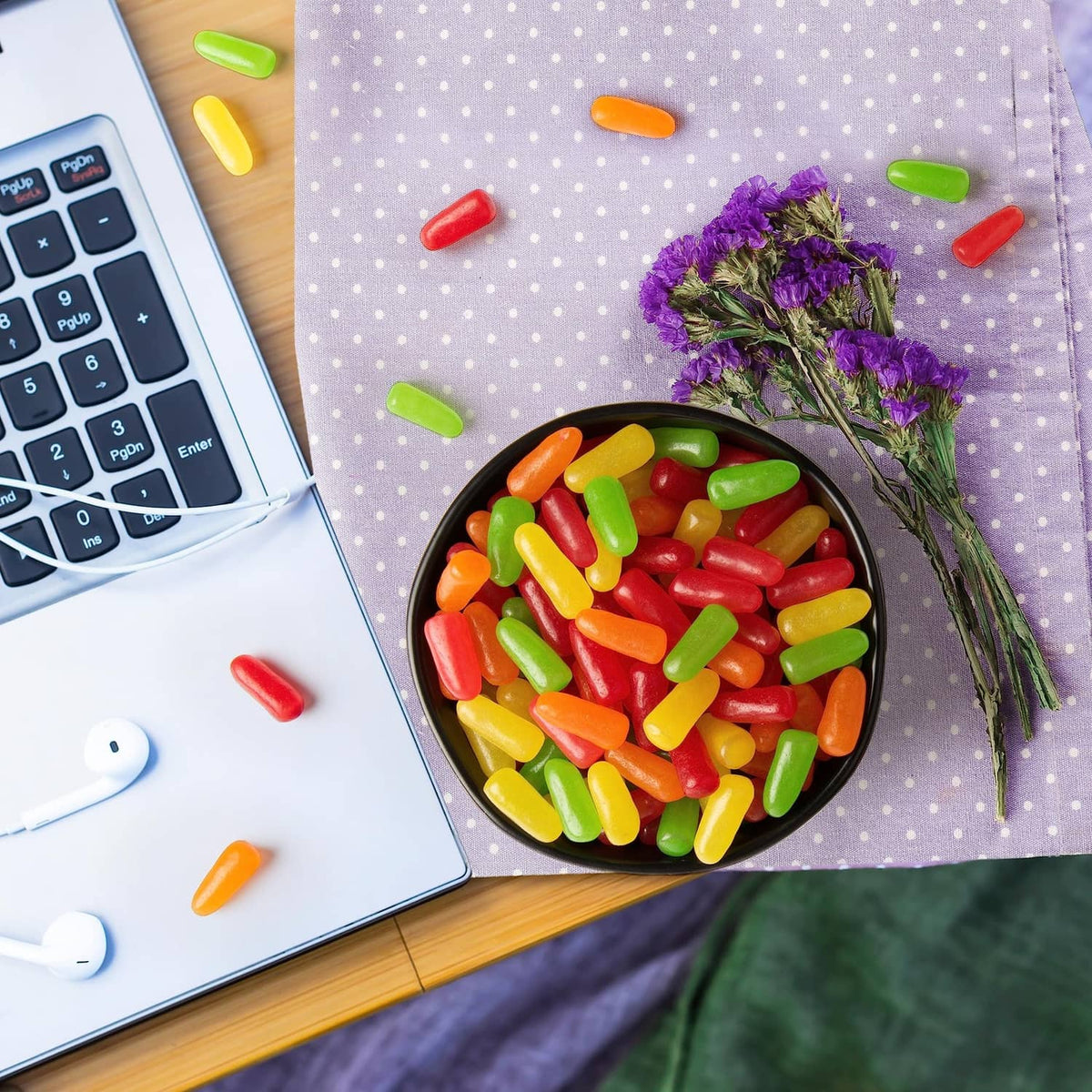Bowl of assorted fruit candy pieces on purple cloth with keyboard and calculator nearby