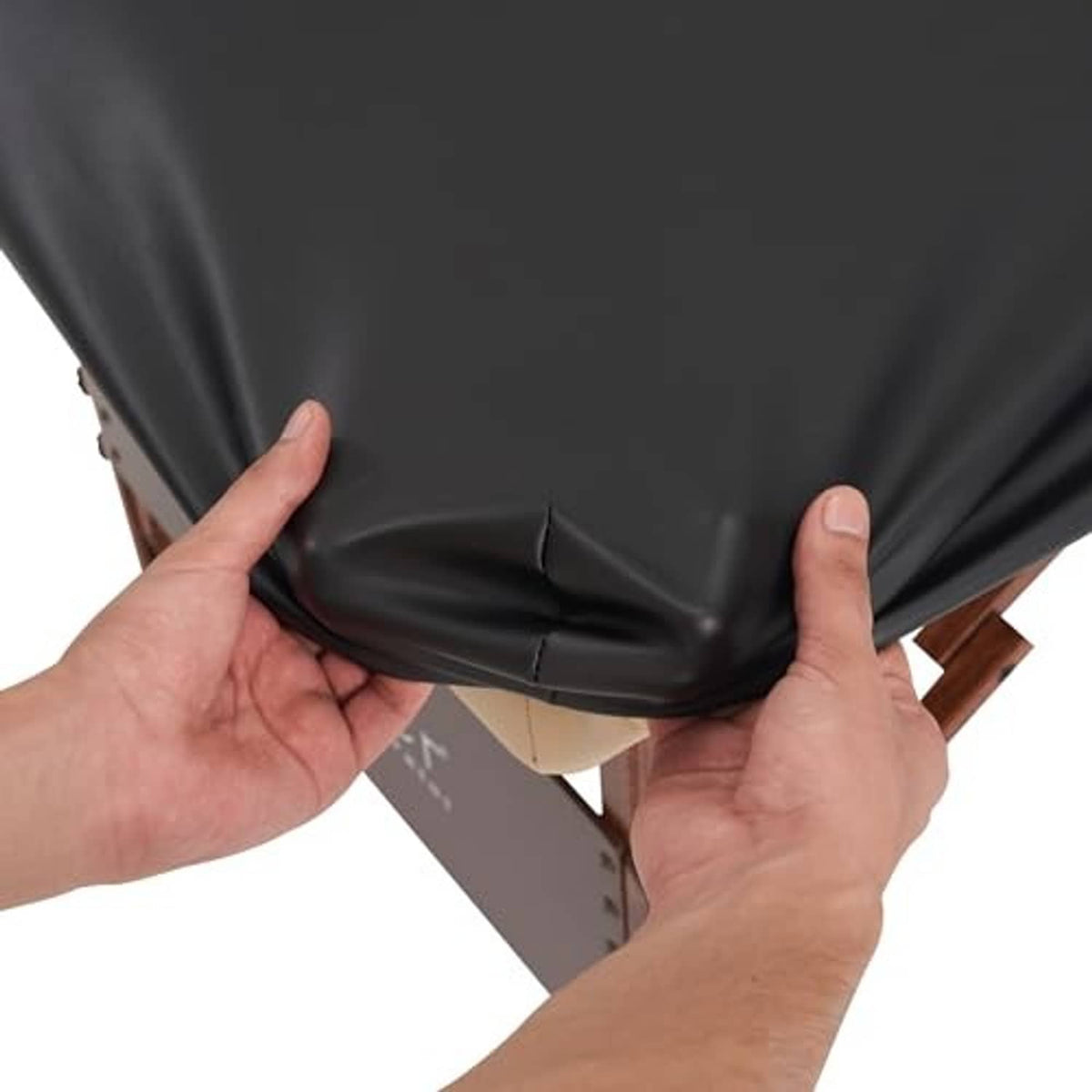 Hands adjusting the fitted edge of a dark PU vinyl massage table cover