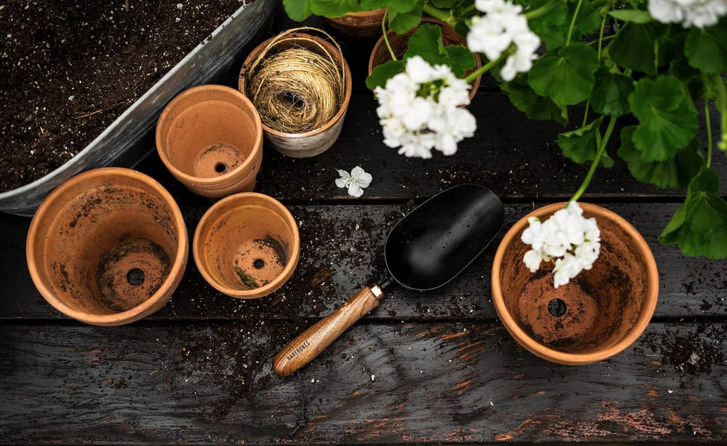 Garden scoop shovel with black scoop and wood handle among terracotta pots and soil