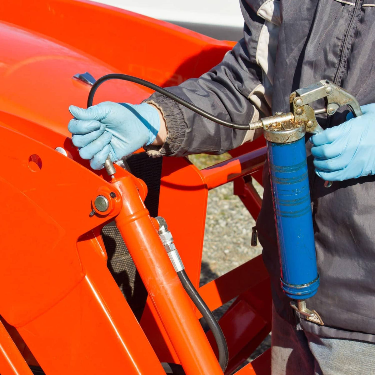 Grease gun hose connected to a grease gun, held by gloved worker