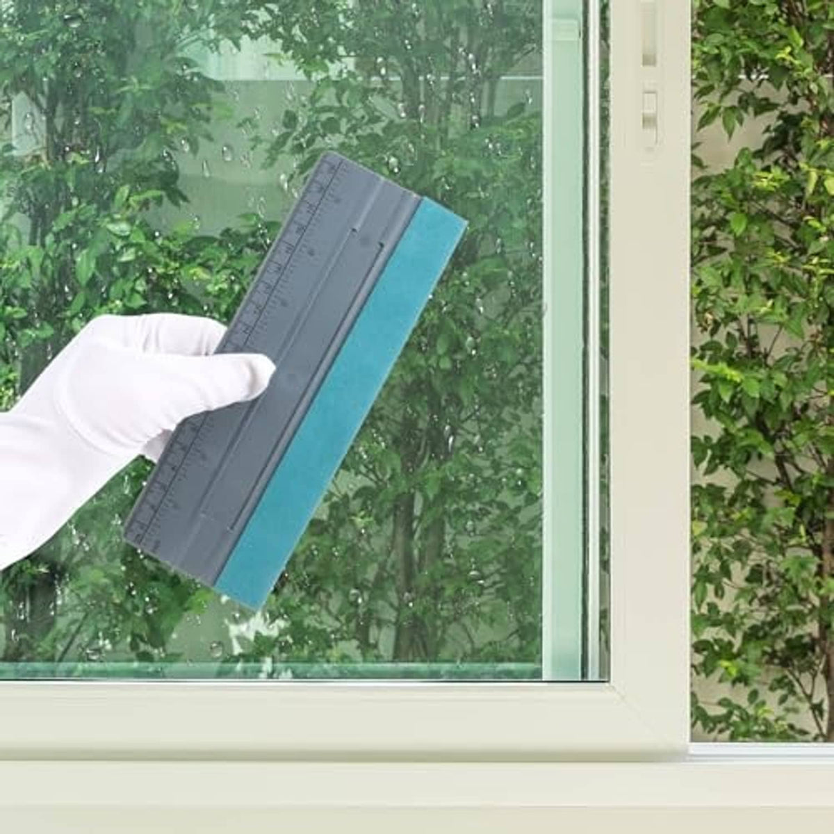 Vinyl squeegee with gray ruler and teal felt pad used on a glass window surface