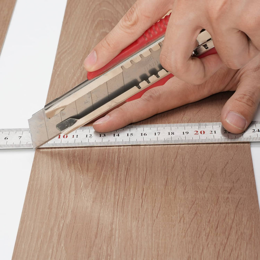 Hand trimming a wood-grain vinyl floor tile plank with a utility knife and ruler