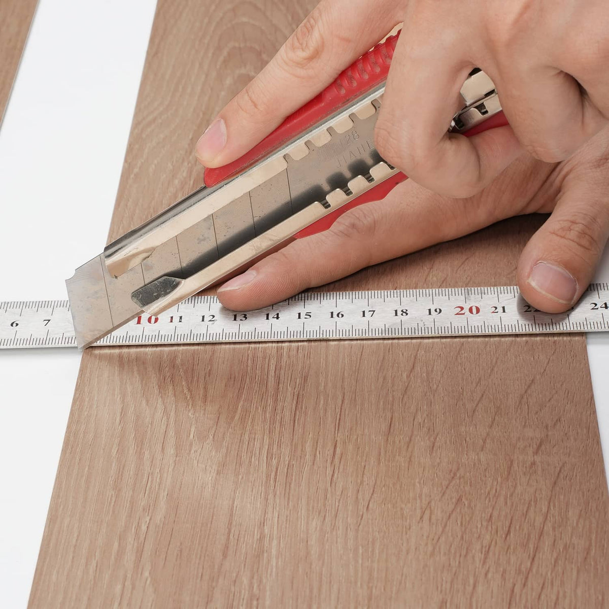 Hand trimming a wood-grain vinyl floor tile plank with a utility knife and ruler