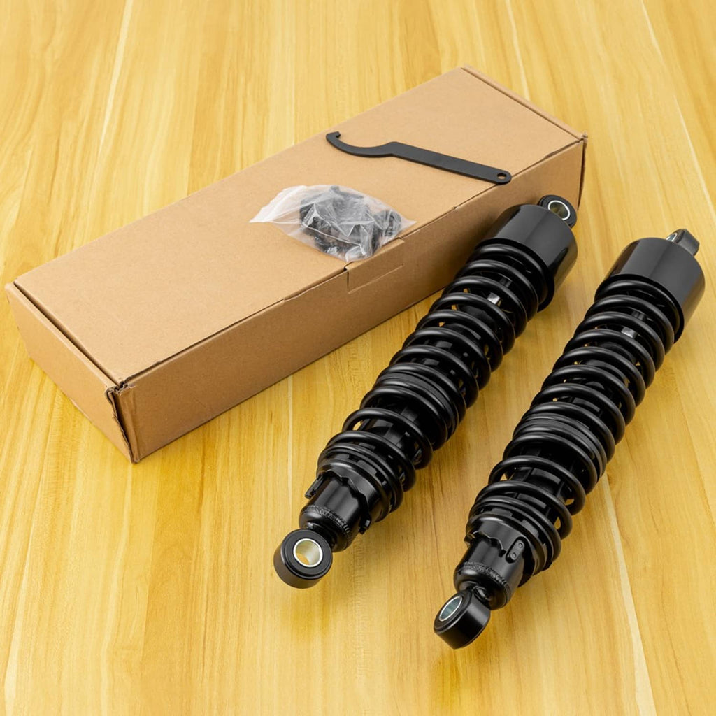 Two black rear shock absorbers with coil springs next to a boxed package and mounting parts