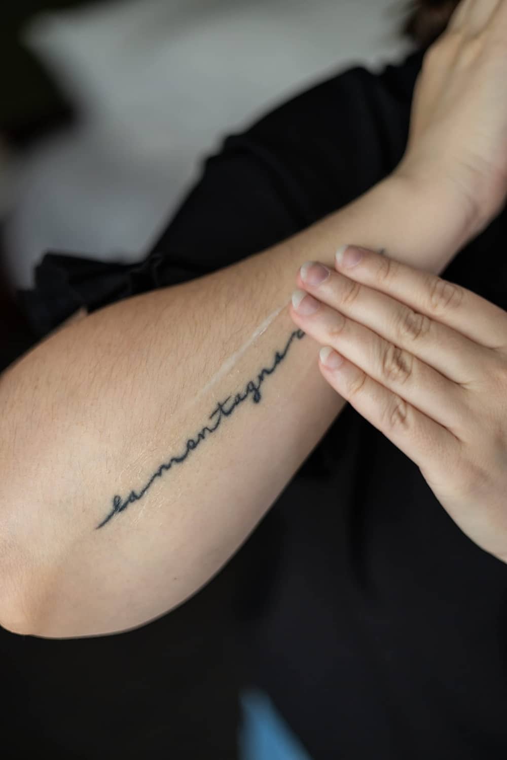 Tattoo care lotion being applied to a forearm with a fine-line tattoo