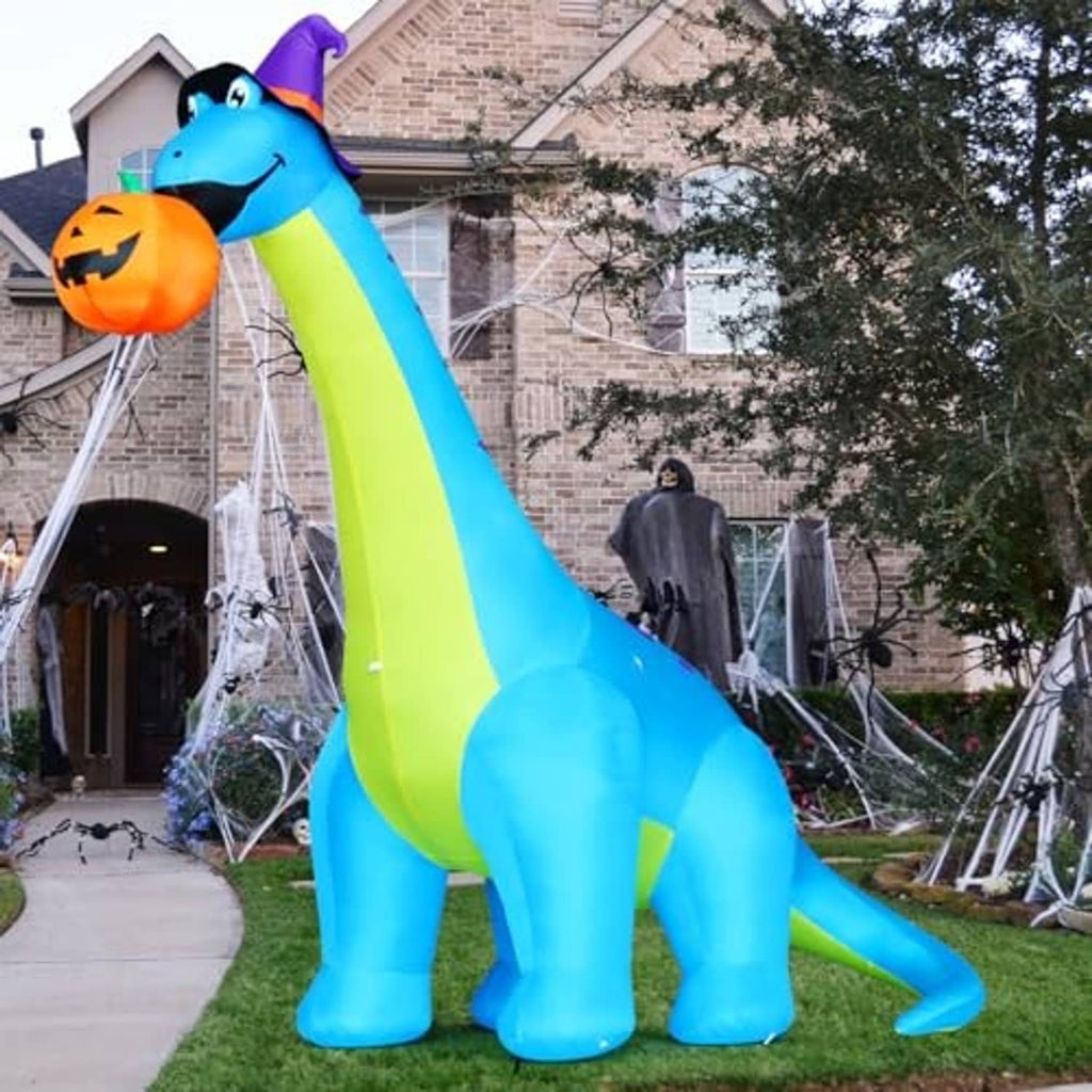Inflatable blue dinosaur with green stripe and purple hat holding pumpkin in yard