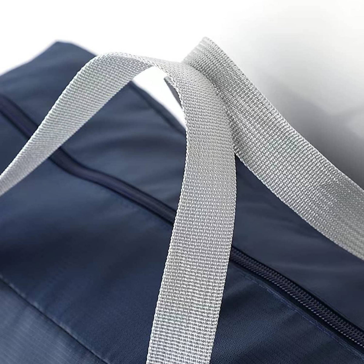 Navy foldable duffel bag with close-up gray webbing strap and zipper seam