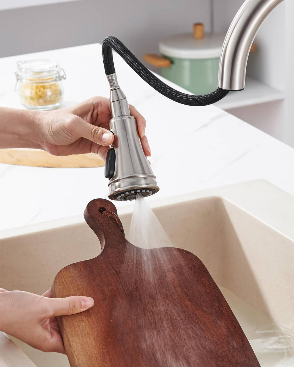 Brushed nickel kitchen faucet sprayer head in use over sink with hose
