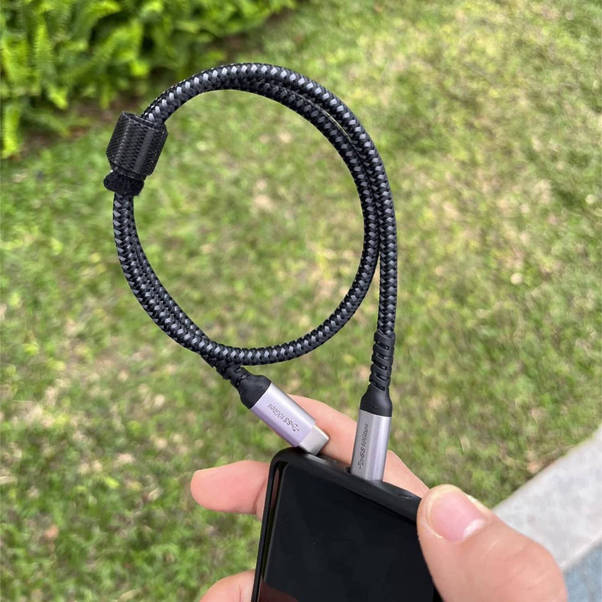 Hand holding braided black USB-C to USB-C cable with silver connector tips