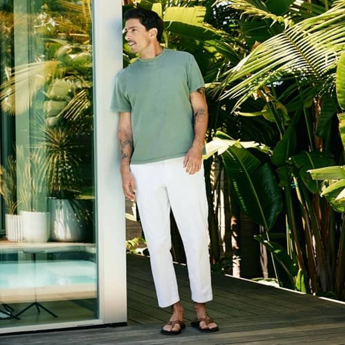 Brown flip-flop sandals with tan thong strap on a man’s feet, worn with white pants.