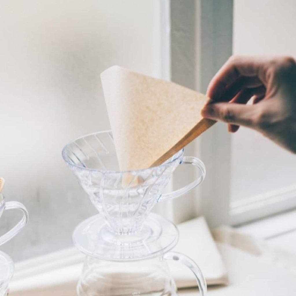 Hand placing a natural cone paper coffee filter into a glass dripper