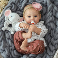 Realistic 18-inch reborn baby girl doll in white heart onesie, brown pants, holding pacifier.
