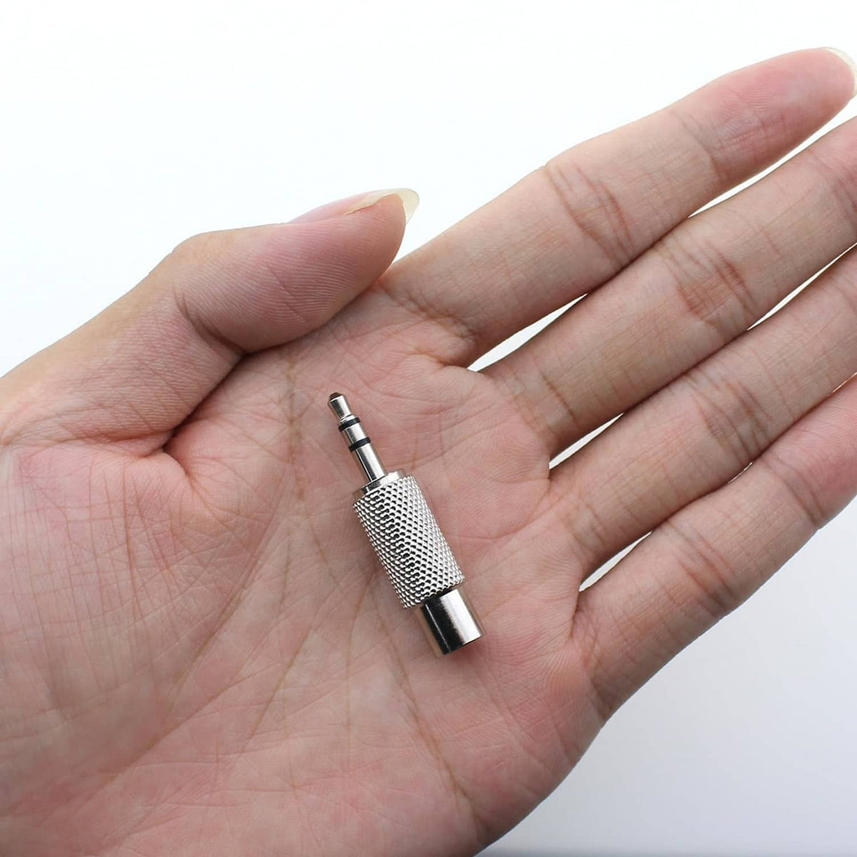 3.5mm stereo male to RCA female adapter held in hand, silver metal plug