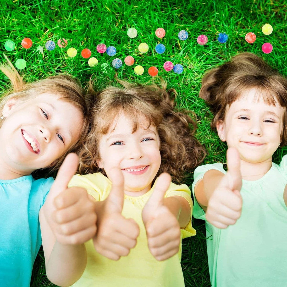 Colorful bouncy balls scattered on green grass as kids pose and point.