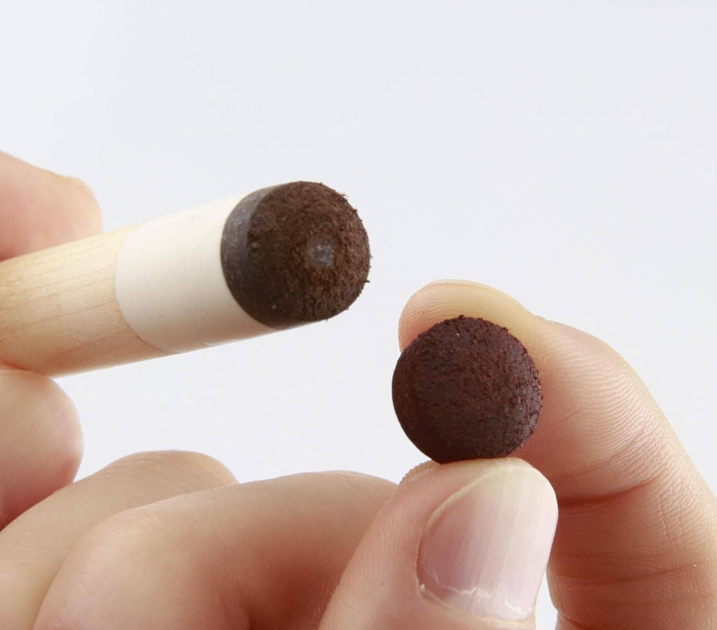 Two dark cue tips held between fingers on a light wooden cue shaft