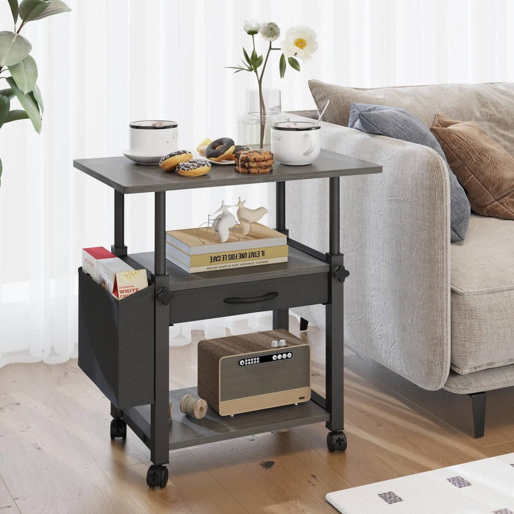 Gray rolling printer stand cart with drawer and two open shelves beside a sofa