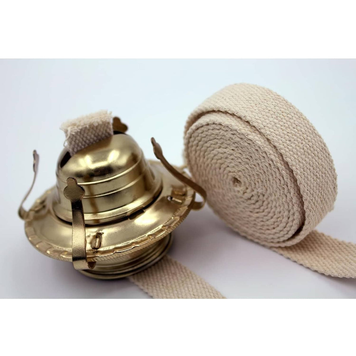 Cotton oil lamp wick roll with blue stitching beside brass oil lamp