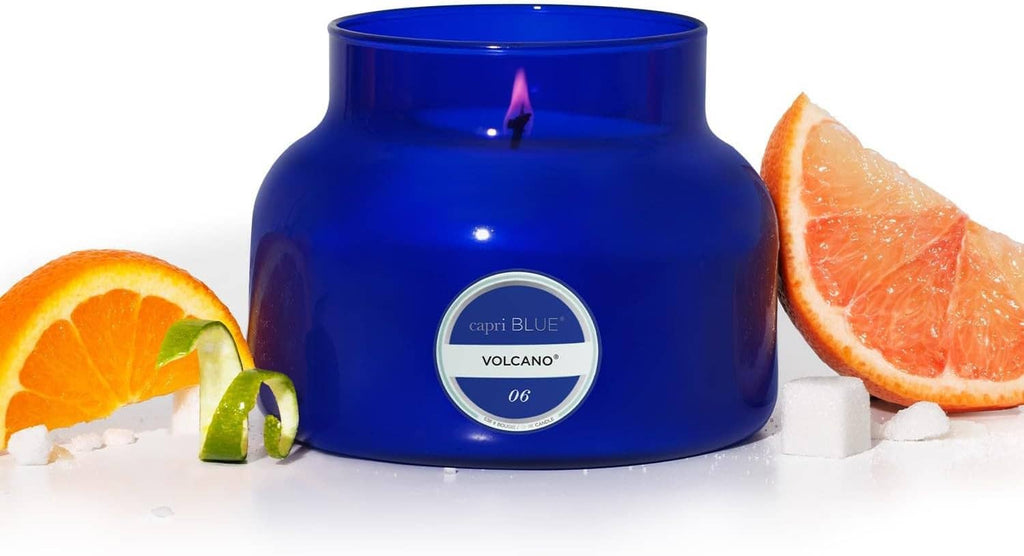 Blue glass jar candle with flame and round label, orange and grapefruit slices nearby