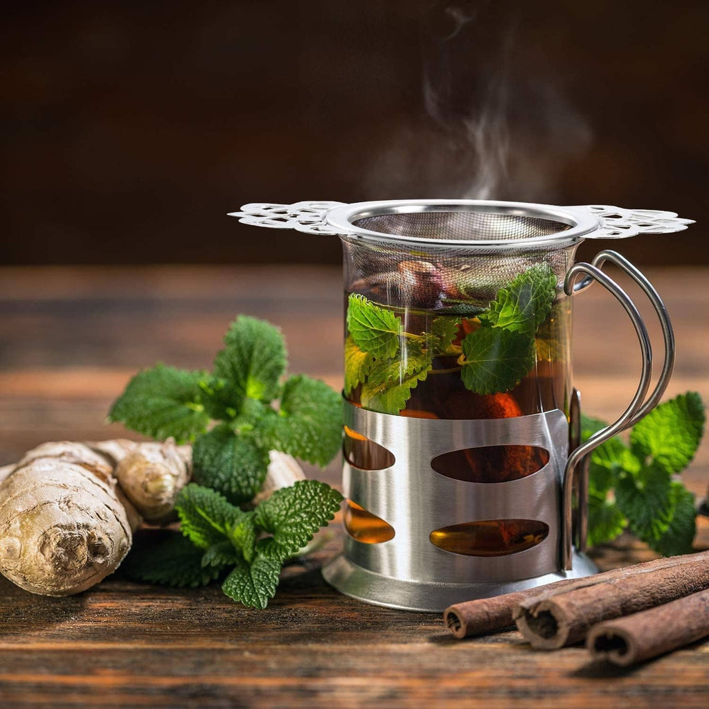 Stainless tea infuser resting on drip bowl while steeping with herbs and mint