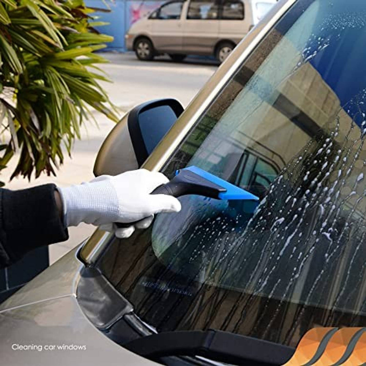Gloved hand holding blue rubber window squeegee with black blade for car window cleaning