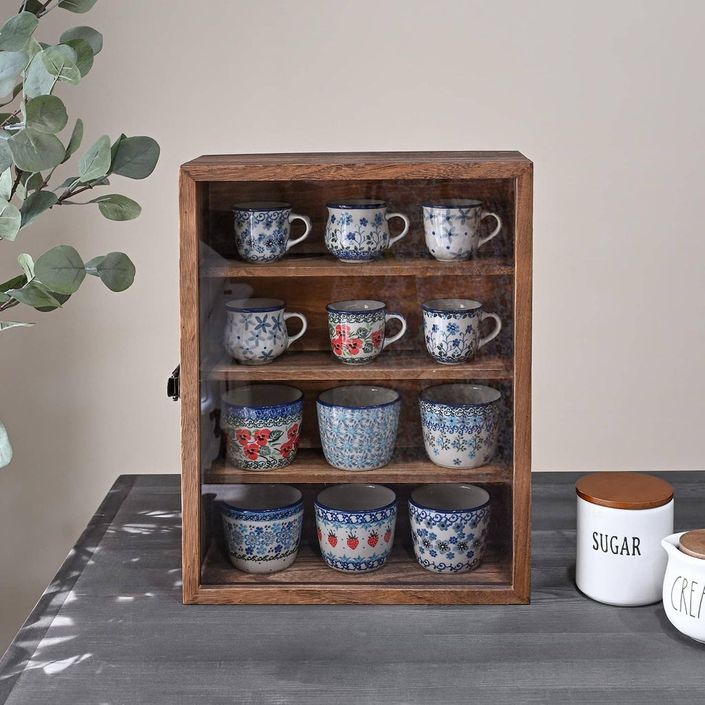 Wooden display cabinet with glass door closed, filled with blue ceramic mugs.