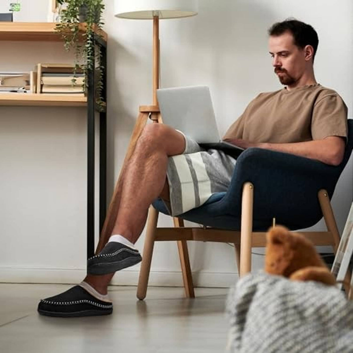 Men's black slip-on indoor slippers with tan lining worn with casual shorts.