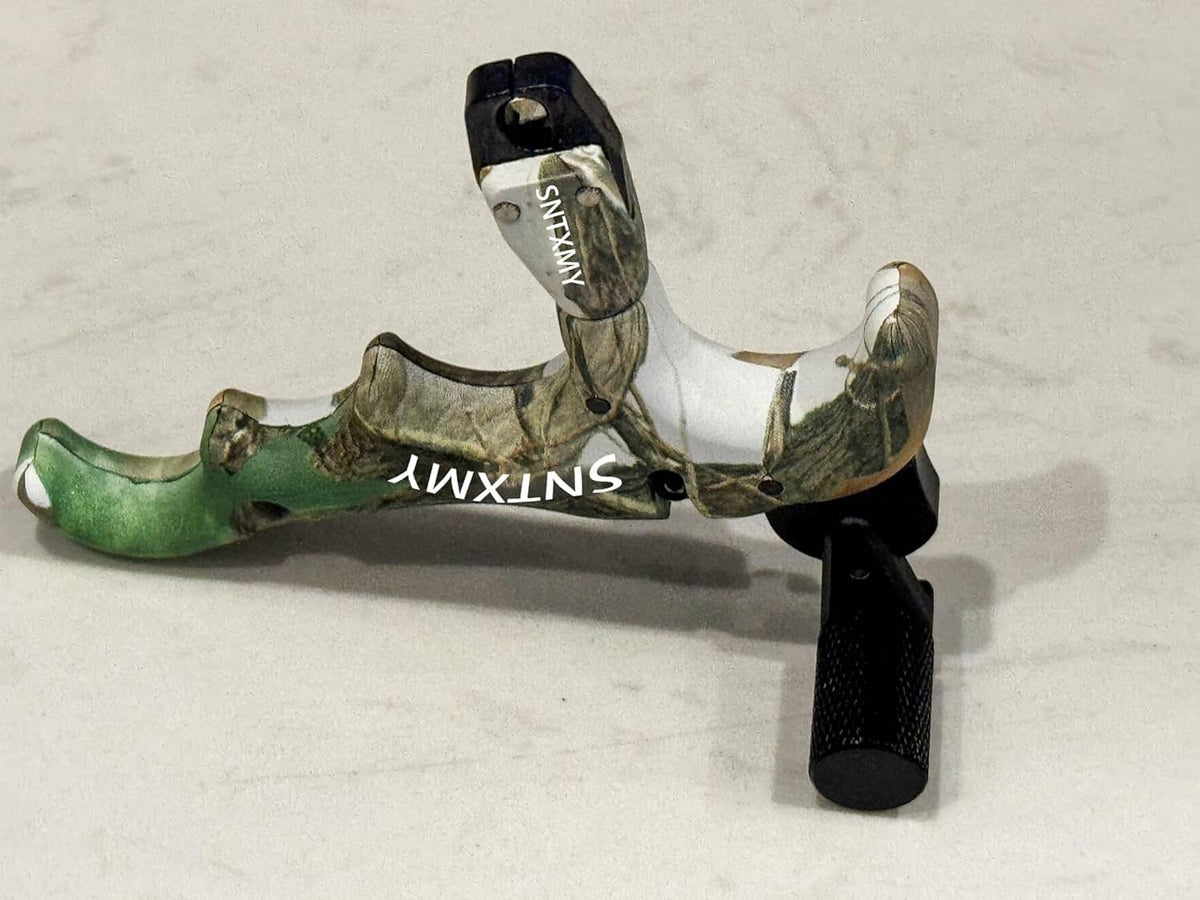 Camouflage thumb bow release with black handle and lanyard loop; metal rod visible.