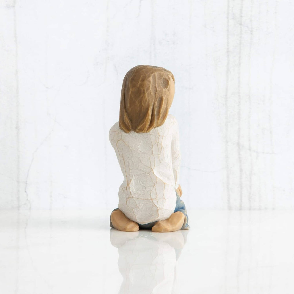 Seated child figurine from behind, brown hair and white robe with blue-gray blanket.