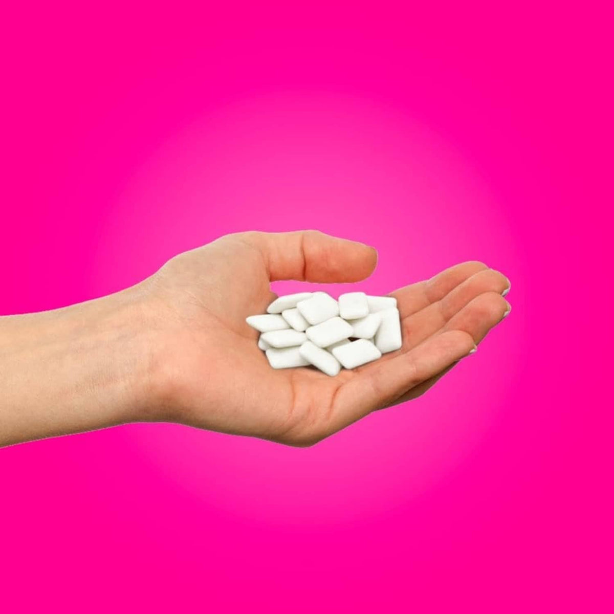 White chewing gum pieces in an open hand, pomegranate mint flavor
