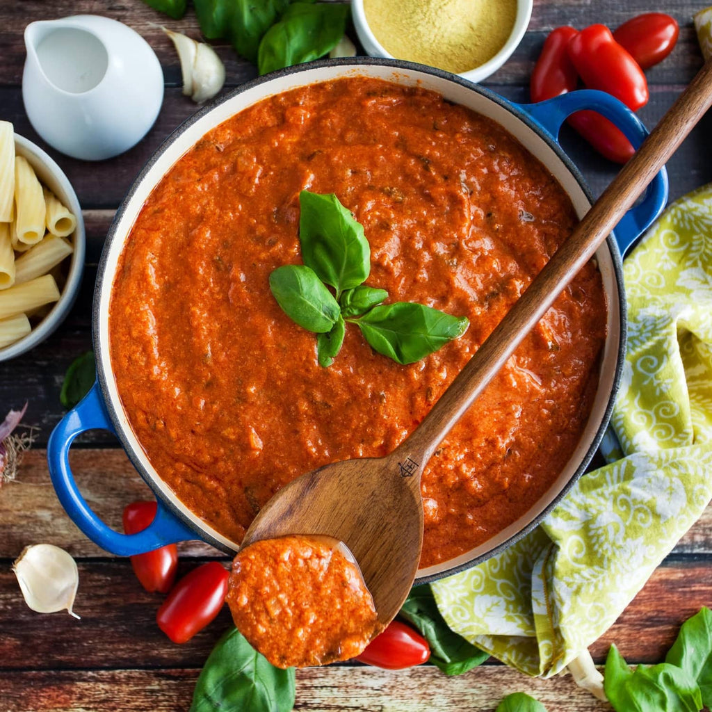Red tomato paste in a blue bowl with basil leaves and a wooden spoon