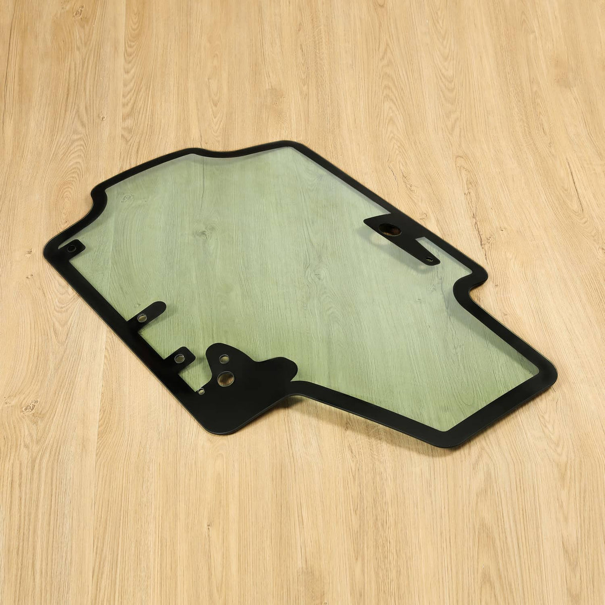 Skid steer door glass panel with black frame and hinge brackets, tinted light green