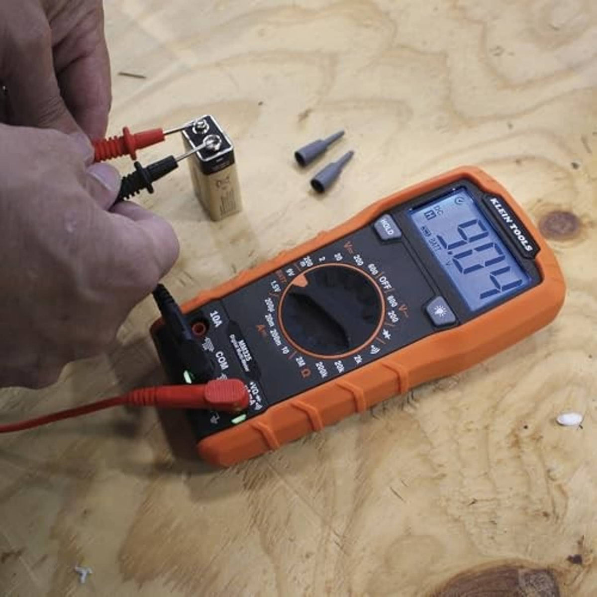 Orange digital multimeter on tabletop with attached red and black test leads and probes.