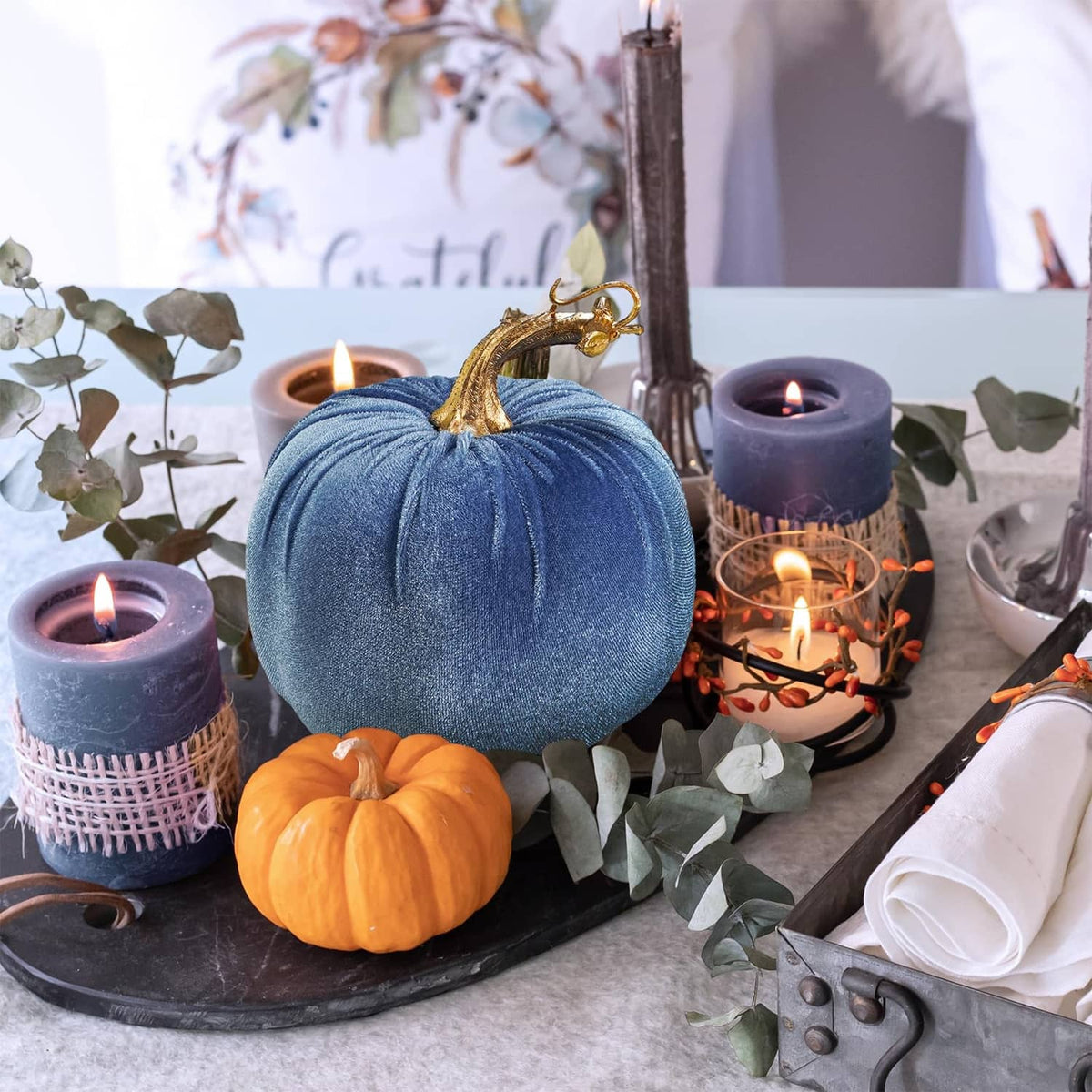Light-blue faux velvet pumpkin with gold stem and hanging loop among fall table decor
