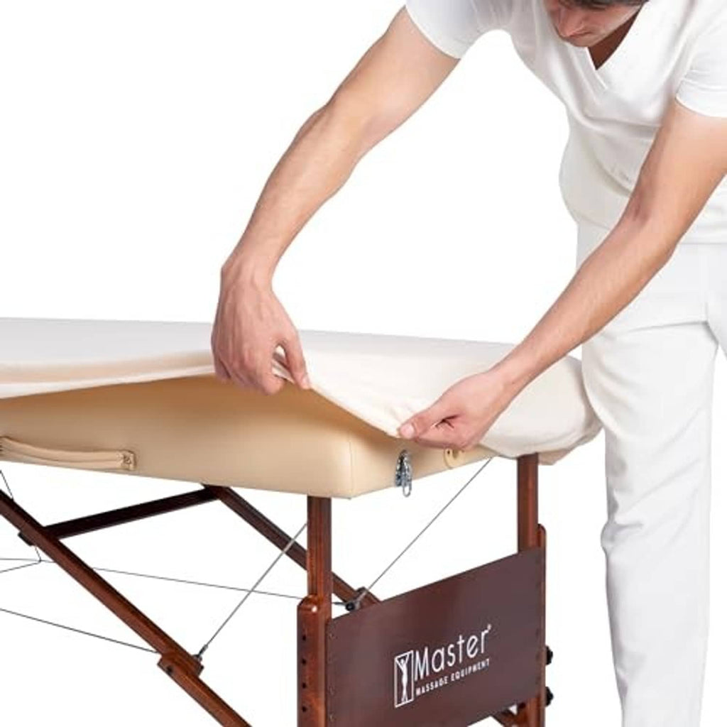 Massage table cover installation: light beige flannel sheet being secured in place.