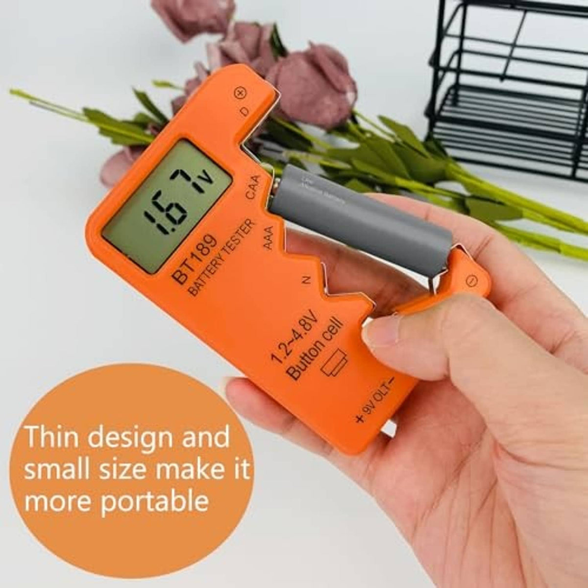 Hand holding orange digital battery tester with LCD reading 6.1V and metal probe