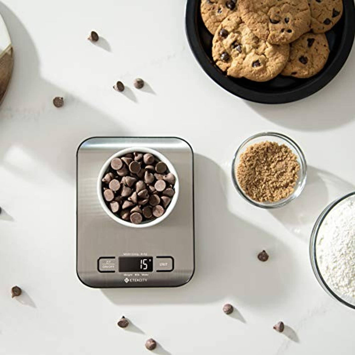 Digital kitchen scale on countertop with chocolate chips and ingredient bowls