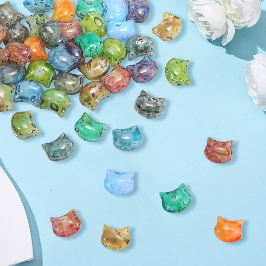 Scattered cat-shaped glass beads in mixed colors on a light blue surface.