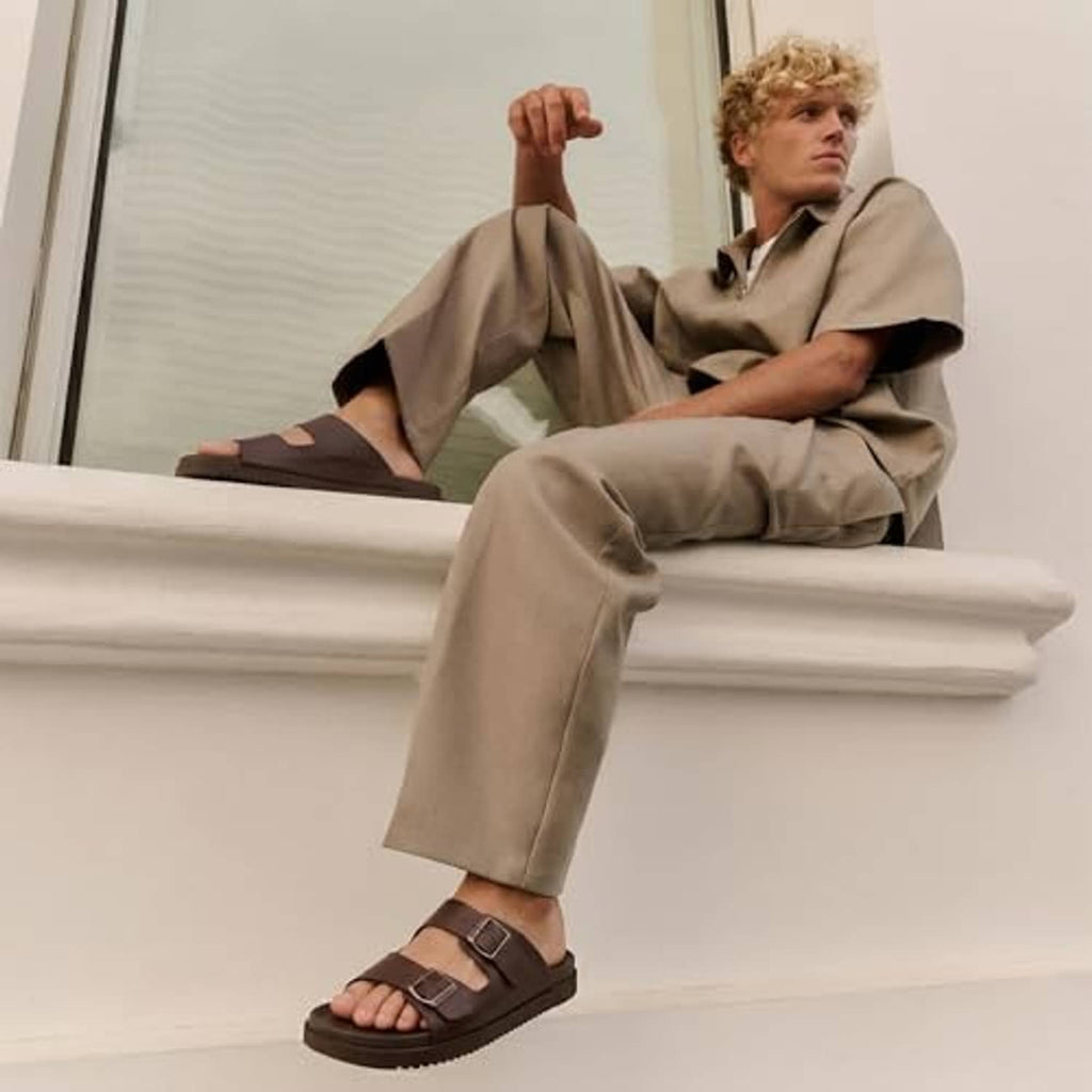 Men's brown adjustable buckle slide sandals worn with beige trousers