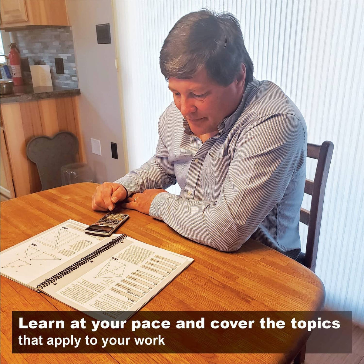 Man reviewing spiral-bound workbook and calculator on a wooden table
