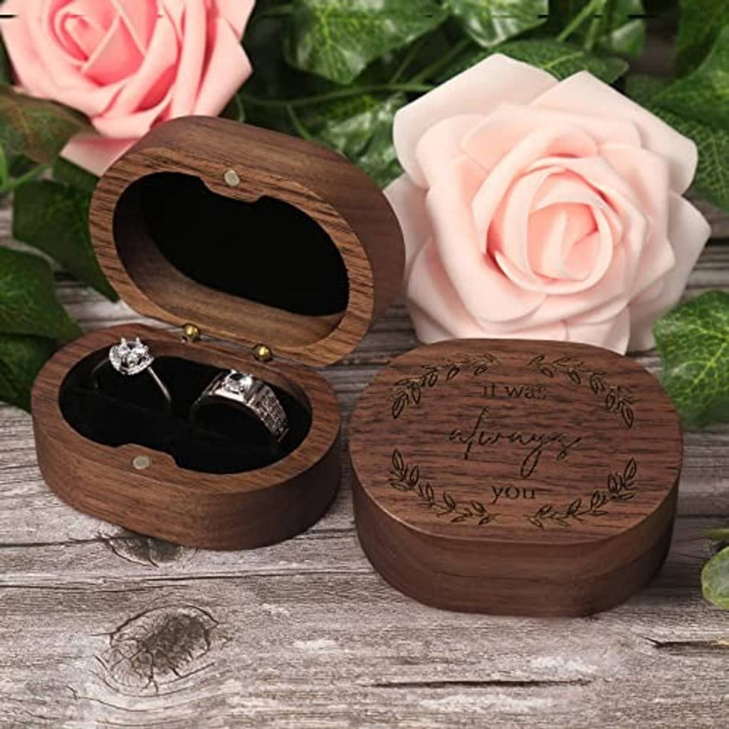 Engraved wooden ring box with oval opening, displaying two engagement rings inside