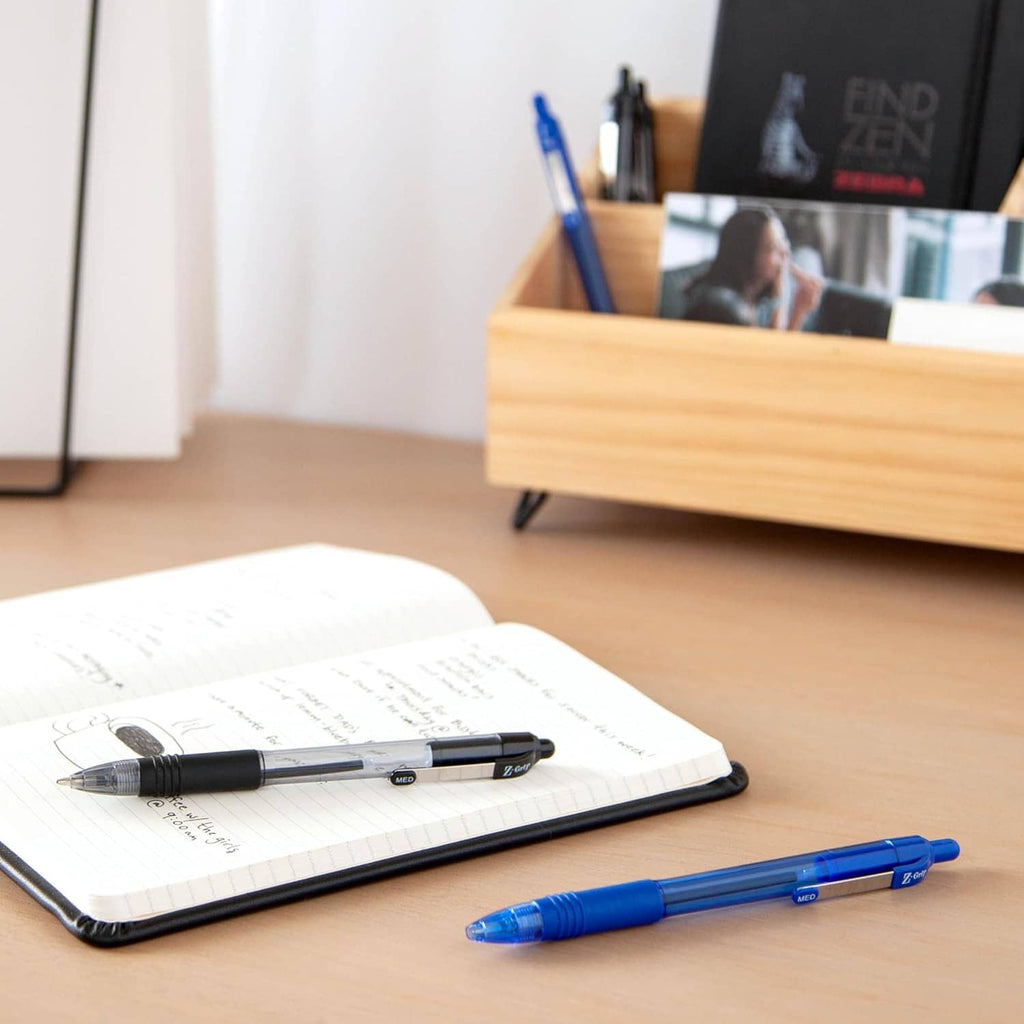 Retractable ballpoint pens on desk with open notebook: black pen and blue pen.
