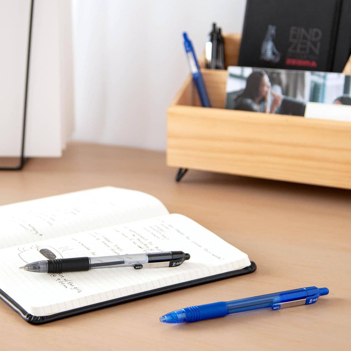 Retractable ballpoint pens on desk with open notebook: black pen and blue pen.