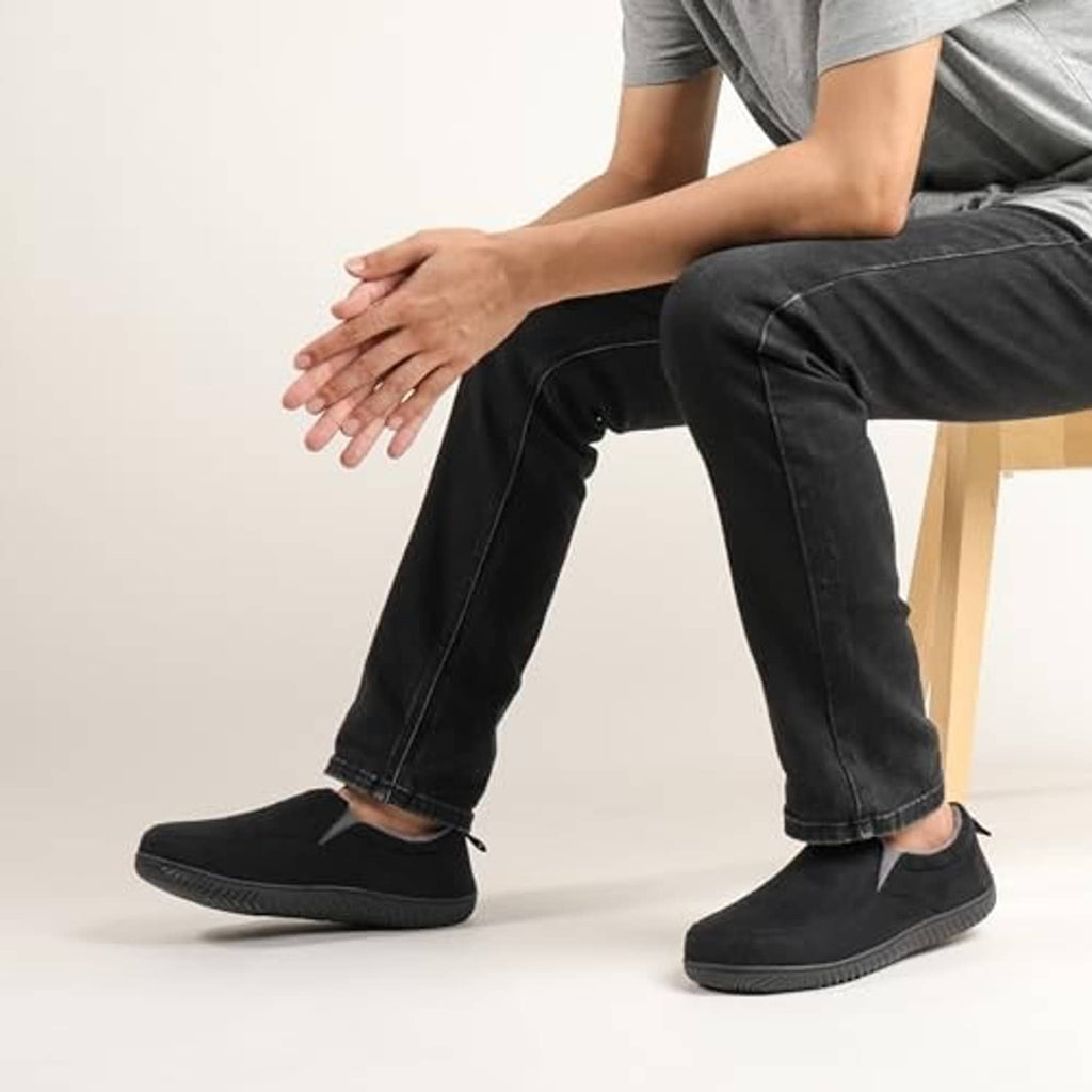 Pair of black closed-back slippers worn with jeans, casual slip-on style.